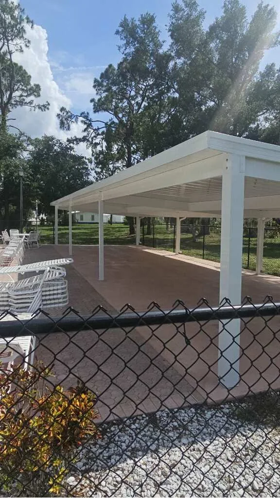 Open-sided white pavilion over a paved outdoor area, viewed from outside the fence