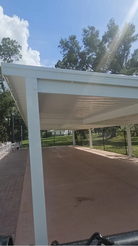 White pavilion roof, beam and support posts above a paved outdoor area.