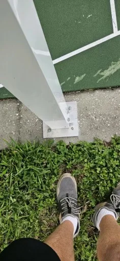 Close-up of a white support post and its base plate beside an outdoor court.